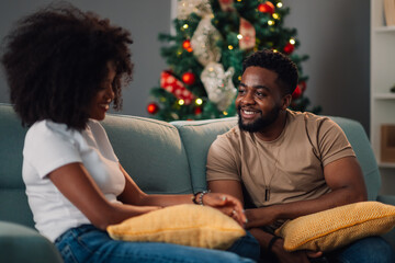 Fototapeta premium African american couple's engaging discussion on teal couch beside Christmas