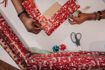 Two people wrapping a Christmas gift with festive decorations.