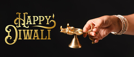 Female hand with diya lamp for celebration of Divaly on dark background