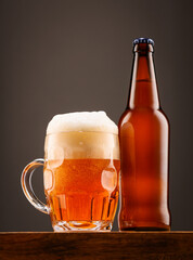 A bottle of beer and a glass of beer on a dark background.