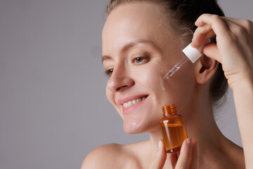 Beautiful young woman applying cosmetic serum onto her face in bathroom. Facial Skincare
