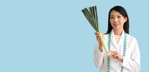 Female Asian nutritionist with leek on blue background with space for text