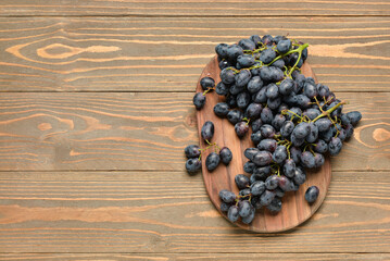Board with sweet black grapes on wooden background