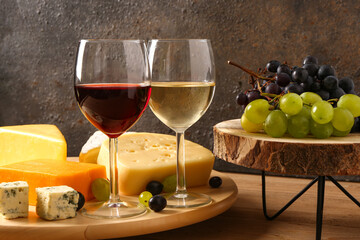 Wooden board with tasty cheese, grapes and glasses of wine on table