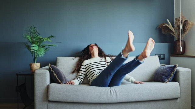 Young woman arriving home from work, throwing herself onto the couch to enjoy a moment of relaxation and comfort. Young woman collapsing onto the couch for a well-deserved break