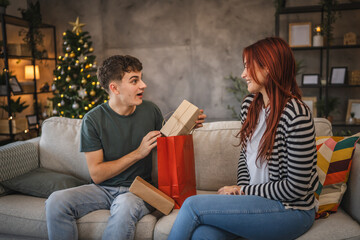 Obraz premium Girlfriend give christmas gift from shopping bag to boyfriend at home