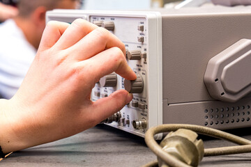 Man hand turns dials on oscilloscope electronic test instrument