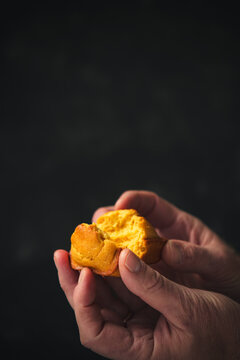 hands open a tiny cornbread muffin in front of a black background