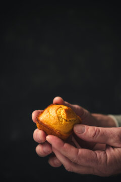 hands hold a tiny cornbread muffin in front of a black background