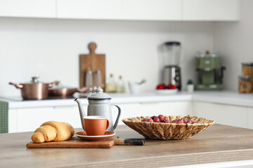 Kitchen table with grapes, cup of tea and croissant in modern kitchen