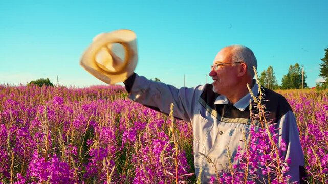Elderly farmer waving his hat in a field of blooming fireweed