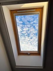 Obraz premium Clear sky view through a skylight reveals a vibrant array of clouds, offering a serene glimpse of outdoors. Wooden frame adds warmth and contrast to the bright blue sky