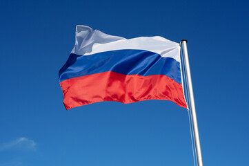 The flag of Russia flutters in the wind against a blue cloudless sky
