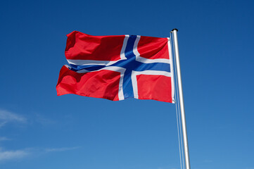 The flag of Norway flutters in the wind against a blue cloudless sky