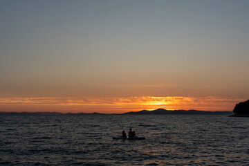 Fototapeta premium Family enjoying sunset paddleboarding on calm sea against a backdrop of hills and glowing sky. Concept of peaceful outdoor adventure, relaxation, and nature appreciation. High quality photo