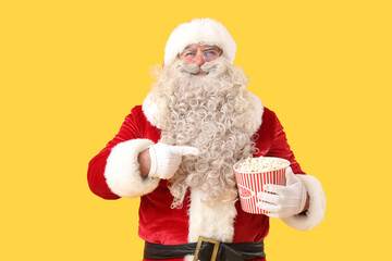 Santa Claus pointing at tasty popcorn on yellow background