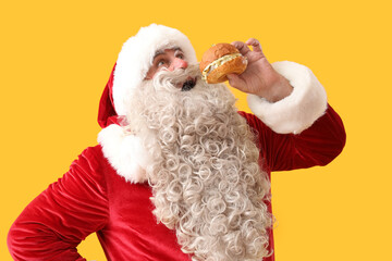 Santa Claus eating tasty burger on yellow background