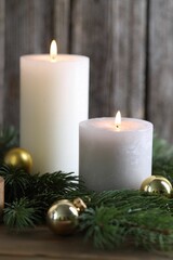 Burning candles, baubles and fir branches on wooden table, closeup. Christmas atmosphere