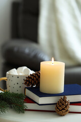 Burning candle, books, fir branches and cones on coffee table indoors, space for text. Christmas atmosphere