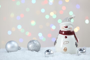 Cute snowman and Christmas balls against beige background with blurred lights, bokeh effect