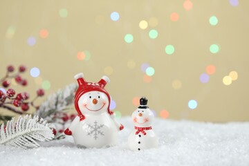 Cute snowmen and other Christmas decor against beige background with blurred lights, bokeh effect