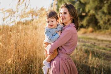 Portrait of happy loving mother hugging her baby son in the sunny park near river