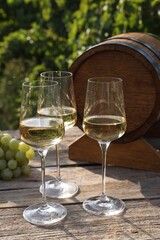Tasty wine in glasses, grapes and barrel on wooden table outdoors