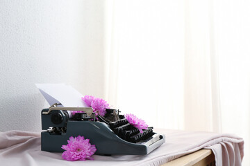Vintage typewriter with paper sheet and flowers on cloth near white grunge wall