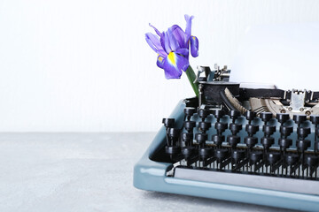 Vintage typewriter with paper sheet and purple flower on grey grunge table near white wall