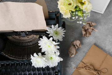 Vintage typewriter with craft paper and flowers on grey grunge background