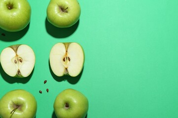 Flat lay composition with whole, cut apples and seeds on green background. Space for text