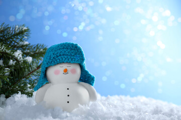 Cute decorative snowman and fir branches on artificial snow against blurred lights. Space for text