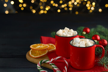 Tasty hot cocoa drinks with marshmallows in cups on black wooden table, closeup. Space for text
