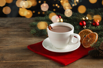 Tasty hot cocoa drink with cinnamon sticks in cup and dry orange slices on wooden table, closeup. Space for text