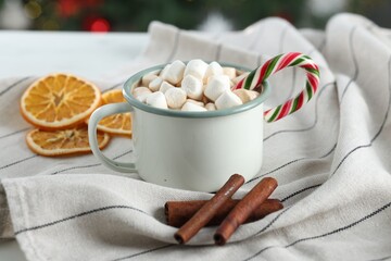 Tasty hot cocoa drink with marshmallows, candy cane in mug and spices on table, closeup