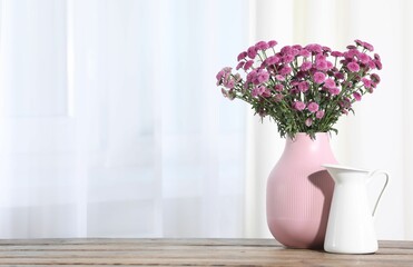 Beautiful pink flowers in vase on wooden table indoors. Space for text