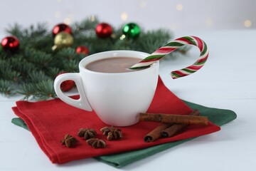 Yummy cocoa and candy cane in cup, spices and Christmas wreath on white wooden table