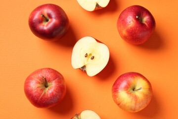 Whole and cut fresh red apples on orange background, flat lay