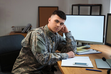 Tired young male soldier sitting at table in headquarters