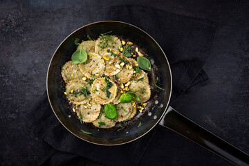Traditional Italian medaglioni pasta staffed with parmesan cheese and pesto served as top view in a rustic frying pan with copy space