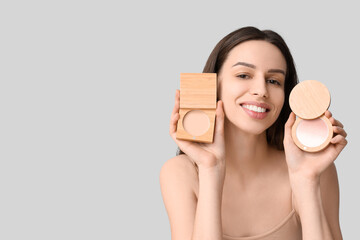 Happy young woman with powder and highlighter on grey background