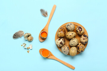 Wooden spoons and board with fresh quail eggs on blue background
