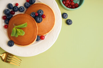 Tasty pancakes with berries on green background