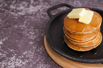 Frying pan with tasty pancakes and butter on grey grunge table