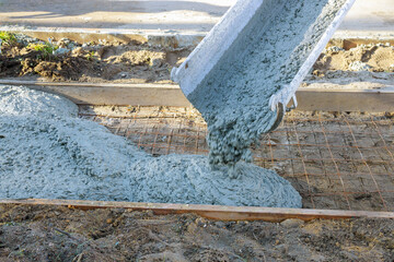 An cement mixing truck pours concrete on reinforced steel bars for construction of new sidewalk