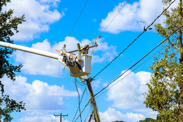 Using utility tower truck, emergency service linemen repair power electrical lines damaged by storm hurricane