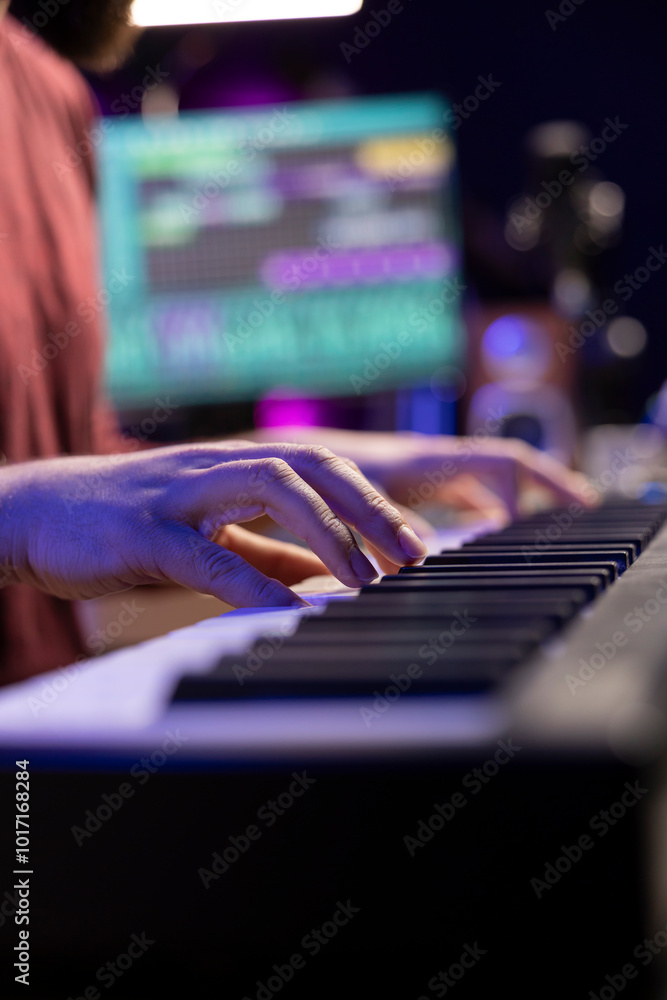 Poster sound engineer playing notes on electronic piano keyboard, creating his personal tunes to use for mi