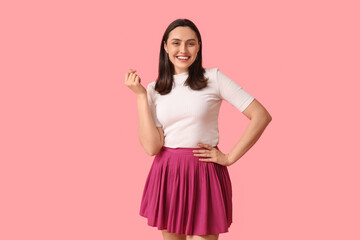 Smiling young woman showing heart gesture on pink background