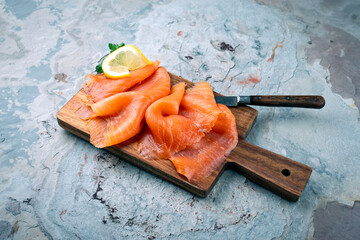 Traditional Norwegian smoked salmon in slices with parsley and lemon served as close-up on rustic...