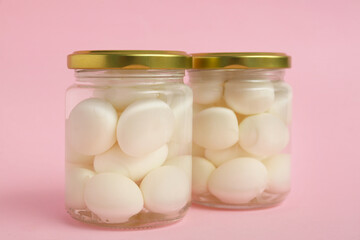 Jars with fresh boiled quail eggs on pink background